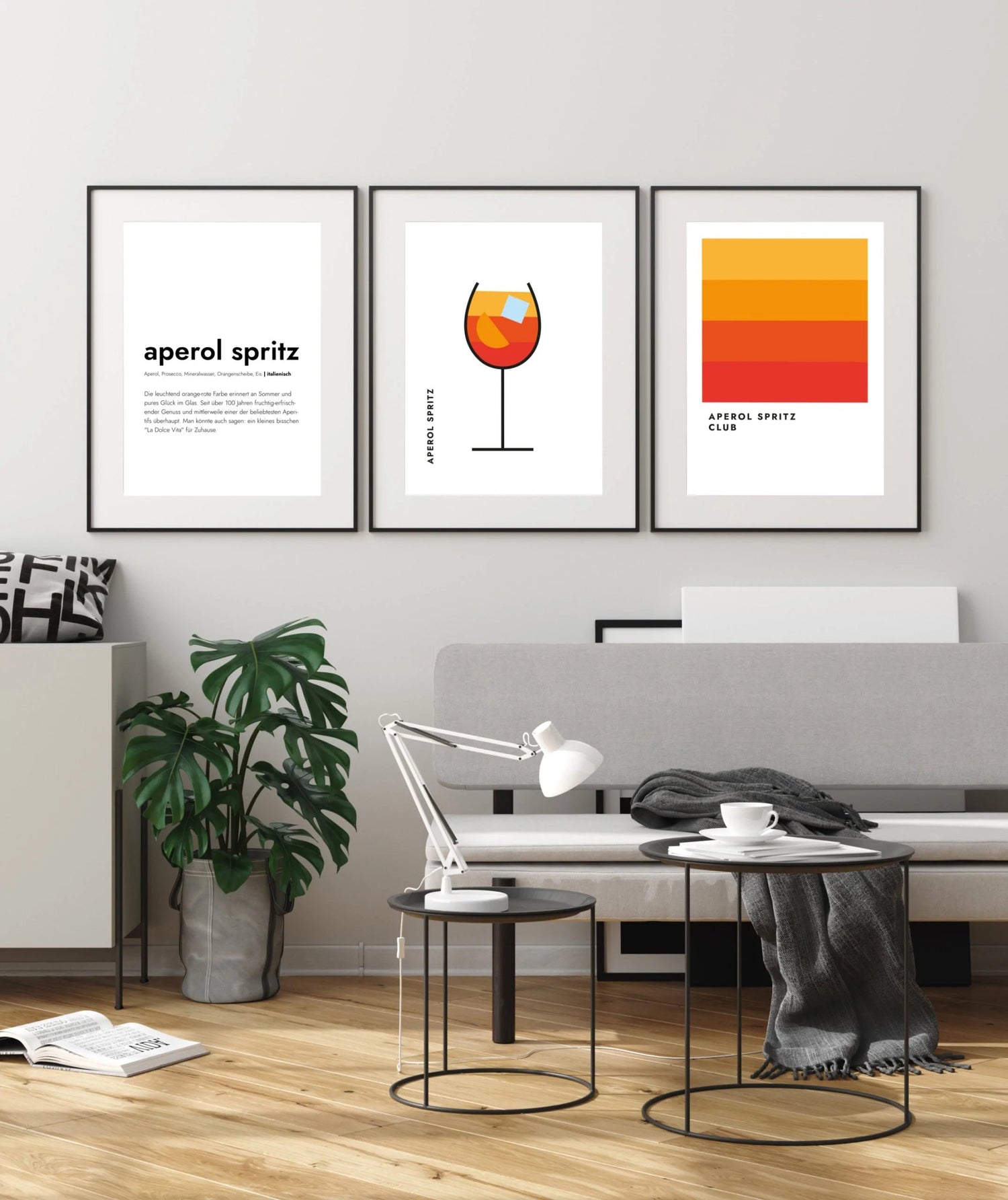 Drei Aperol Spritz Poster im Bilderrahmen im Wohnzimmer, dadrunter eine Couch mit Tisch und Leselampe
